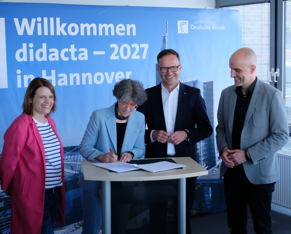 Gruppenbild, Menches stehen ane einem Pult, eine Frau unterzeichnet ein Papier